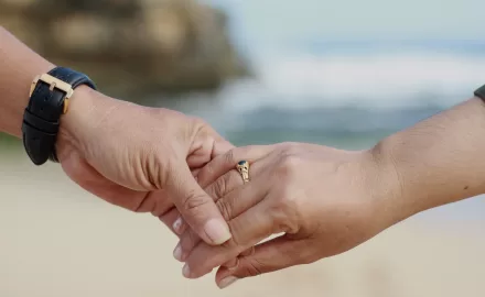Casal de mãos dadas usando aliança de ouro no casamento