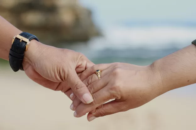 Casal de mãos dadas usando aliança de ouro no casamento